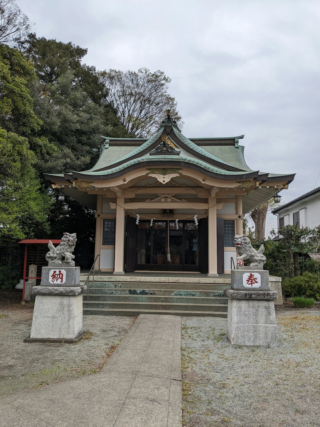 木々の下、狛犬が立つ神社の風景。
